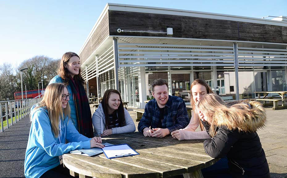 a group of students sat around a table outside laughing 