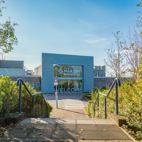The main entrance of Plymouth Marjon University surrounded by greenery and blue skies